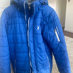 Blå skidjacka Peak Performance - Blå fodrad skidjacka från Peak Performance med huva i strl L. Vind- och vattentålig. Ficka för liftkort.