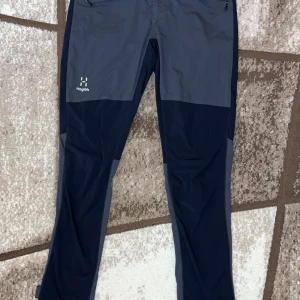 Svart och grå friluftsbyxor Haglöfs - Snygga friluftsbyxor från Haglöfs i svart och grått, dammodell i storlek 36. Byxorna har raka ben, dragkedjor vid fickorna och är tillverkade i slitstark syntet. Perfekta för utomhusaktiviteter och äventyr.