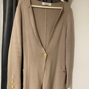 Beige cardigan jacka från Chiara Forti - Snygg beige cardigan jacka från Chiara Forti Milano med guldfärgade knappar fram och på ärmsluten. Jackan är stickad, har lång ärm och två fickor framtill. Perfekt för dig som gillar stilrena och klassiska plagg med exklusiva detaljer. Köpt för ungefär 1300 kr, pris kan diskuteras.