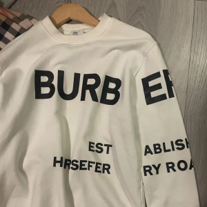 Burberry sweatshirt Limited edition  - Vit sweatshirt från Burberry med stora svarta bokstäver och grafiskt tryck på bröstet och ärmarna. Tröjan har rund hals och lång ärm, tillverkad i mjuk bomull. Perfekt för dig som gillar statement-plagg och exklusiva märken.
