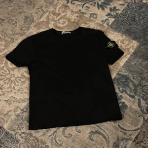 Svart  t-shirt med patch - Svart t-shirt med rund hals och ikonisk avtagbar patch på vänster ärm. T-shirten är i mjuk bomull och har en clean, stilren look som passar perfekt till streetwear. Snygg och enkel att matcha med jeans eller shorts.
