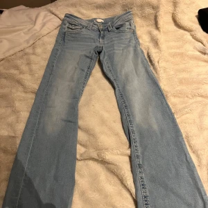 Ljusblå jeans med raka ben - Snygga ljusblå jeans med klassisk femficksdesign och raka ben. Jeansen har detaljerade bakfickor med lock och knapp, samt slitningar framtill för en cool look. Perfekta för dig som gillar en avslappnad stil.