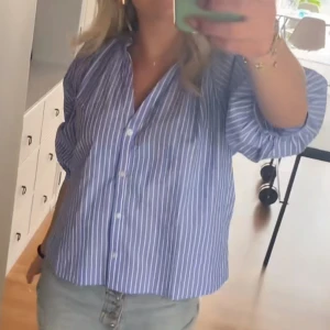 Blårandig blus - Blårandig blus från H&M i storlek XS. Blusen har en loose passform, klassisk krage och knappar framtill. Tillverkad i mjuk bomull med vita vertikala ränder och långa ärmar som kan rullas upp. Perfekt för en chill och stilren look.