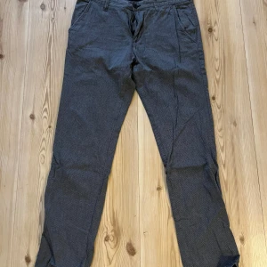 Tom Tailor straight chinos blå W32 L32 - Snygga blå straight chinos från Tom Tailor i storlek W32 L32. Byxorna har ett diskret mönster, klassisk passform med raka ben och sidofickor fram samt bakfickor. Perfekt för dig som gillar stilrena och bekväma byxor.