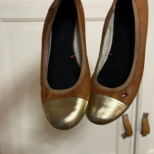 Bruna Tommy Hilfiger ballerina skor - Balla bruna Tommy Hilfiger ballerina skor med guld framtill. 