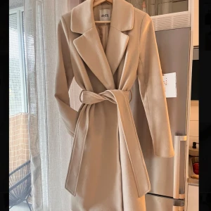 Sandbeige kappa från mByM - Snygg och stilren kappa från mByM. Kappan är i bra skick utantill, dock är den sliten på insidan vid armhålan där en reva är sydd 🧵🪡 Nypriset är 2200kr, pga inte helt i nyskick säljer jag denna för 500kr 💞 Färgen är sand/grå beige! Material: ullblandning, 50% ull 45%polyester 5% andra fibrer, håller värme superbra! 