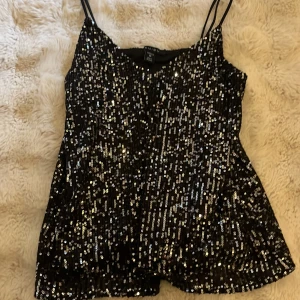Svart glittrig paljettopp från Amisu - Säljer en svart glittrig topp från Amisu i storlek XS. Toppen har tunna axelband och är täckt med paljetter som ger ett riktigt snyggt och festligt intryck. Perfekt för dig som vill sticka ut med lite extra bling. Materialet är syntet och toppen är ärmlös.