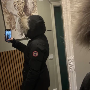 Svart dunparkas Canada Goose - Säljer en svart dunparkas med stor huva och fluffig päls runt kanten, i befintligt skick. Fin & varm! Otroligt Skön att ha på vintern. Finns även så man kan dra åt i midjan och justera själv! Passar nog allt från S-L.