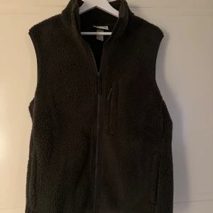 Mörkgrön fleeceväst från HM med dragkedja - Mysig mörkgrön fleeceväst från HM med hög krage och hel dragkedja framtill. Västen har en praktisk bröstficka med dragkedja och är tillverkad i mjuk fleece som håller dig varm. Perfekt att slänga på över en hoodie när det är kyligt ute.