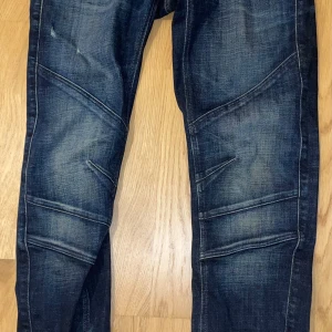 Mörkblå jeans från G-Star RAW - Säljer ett par mörkblå jeans från G-Star RAW med coola sömdetaljer över benen och bakfickor med broderad båge. Jeansen har klassisk femficksdesign, normal passform och slitningar för en schysst streetkänsla. G-star raw snygga herr jeans (moto cross 3d) W30 L32