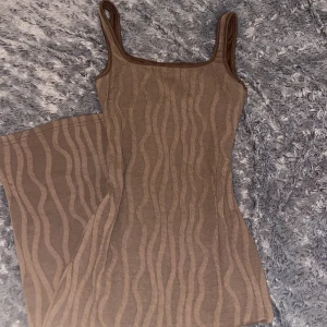 Brun långklänning med vågigt mönster - Snygg brun långklänning från SHEIN i storlek XS. Klänningen har ett vågigt mönster, smala axelband och figurnära passform. Materialet är mjukt och stretchigt, perfekt för dig som gillar en stilren look med lite edge.