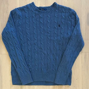 Blå kabelstickad tröja Polo Ralph Lauren🤩 - Snygg blå kabelstickad tröja från Polo Ralph Lauren i storlek S. Tröjan har rund hals, ribbade muddar och det klassiska broderade Polo-logot på bröstet. Perfekt för dig som gillar en clean och tidlös look.