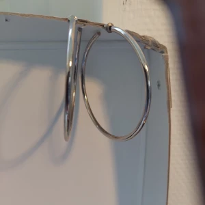 Stora silvriga hoops örhängen - Säljer ett par stora, klassiska hoops i silverfärgad metall. De är runda och har en stilren, minimalistisk design som passar perfekt för dig som gillar enkla men snygga accessoarer. Ca 7 cm i diameter