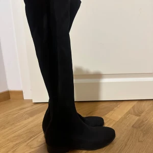 Svarta stövlar precis under knäna - Snygga svarta stövlar precis under knäna i mjuk mocka med platt sula och rund tå. Perfekta för att lyfta vilken outfit som helst och ger en stilren look. Stövlarna har en klassisk design och passar till både kjol och jeans. Använts en gång 