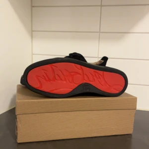 Christian Louboutin svarta  - Säljer ett par svarta sneakers från Christian Louboutin i lyxig mocka med ikonisk röd sula och snörning. Skorna har en stilren design med rund tå och diskreta detaljer, perfekt för dig som vill sticka ut med exklusiv känsla. Kommer med originalkartong och dustbag.