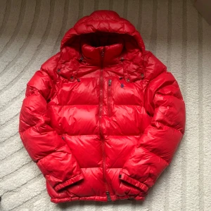 Ralph Lauren puffer jacka - Snygg, varm och skön Ralph Lauren jacka i en sällsynt röd förg. Jackan är i fint skick. Det finns 2 små defekter. Hör av er till mig så skickar jag bild på dessa. Storlek: M