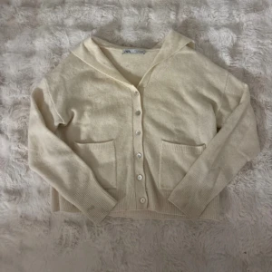 Beige kofta med sjömanskrage från Zara - Superfin beige kofta från Zara med unik sjömanskrage och stora ribbade muddar. Koftan har knappar framtill och två praktiska fickor. Perfekt för lager-på-lager och ger en chill men ändå stilren vibe.