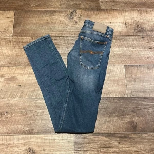 Blå jeans från Nudie Jeans - Snygga blå jeans från Nudie Jeans med klassisk femficksdesign och kontrastsömmar på bakfickorna. Jeansen har en rak passform och normal midja, tillverkade i slitstarkt bomullsmaterial. Perfekta för dig som gillar stilrena och tidlösa jeans.