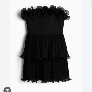 Svart axelbandslös volangklänning - Aldrig använd med lappen kvar!! ❣️originalpris 800kr Supersnygg svart axelbandslös klänning med volanger upptill och i två lager på kjolen. Klänningen har en kort och figurnära passform med romantiska detaljer och en lätt, luftig känsla.