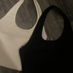 Svart och vit linnetopp, ärmlös - Två stilrena linnetoppar i svart och vitt med klassisk racerback-design. Båda är ärmlösa och har rundad halsringning, perfekta för att matcha med jeans eller shorts. Materialet känns mjukt och stretchigt, vilket gör dem sköna att bära hela dagen.