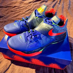 Nike KD 4 NERF (2024) - Säljer ett par Nike KD 4 NERF (2024) som nästan aldrig använts. Skokartong följer med. Färgstark design i blått, rött, grönt och grått. Skorna har kardborreband över vristen och grafiska detaljer. Sulan är röd och grön med mönstrad struktur. Någon fundering? Bara att skriva och fråga.