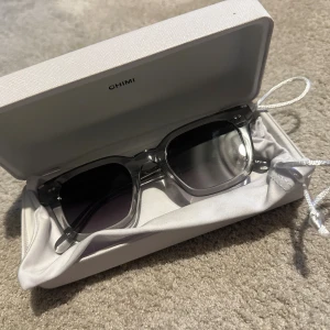 CHIMI transparenta solglasögon - Snygga solglasögon från CHIMI med transparent fyrkantig båge och mörkgrå tonade linser. Kommer med vit hård förvaringsbox och mjukt tygfodral. Perfekt accessoar för att lyfta din stil under soliga dagar. Priset kan diskuteras💕