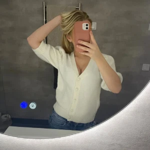 Vit stickad kofta med v-ringning - Säljer en vit stickad kofta med v-ringning och knappar framtill. Koftan har trekvartsärm och ribbade muddar vid ärmslut och nederkant. Perfekt att slänga över en topp och matcha med jeans för en chill look.