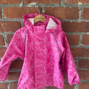 Rosa regnjacka med kronmönster Line One - Säljer en rosa regnjacka från Line One med coolt kronmönster över hela jackan. Jackan har huva, långa ärmar och stängs med knappar framtill. Perfekt när du vill sticka ut i regnet och hålla dig torr.