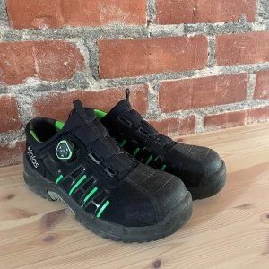 Svarta Jalas sneakers med gröna detaljer - Säljer ett par svarta Jalas sneakers med gröna detaljer och BOA-snörning. Skorna har robust sula, rund tå och insida i grått och grönt. Perfekta för dig som vill ha en grym sko som är snygg och grym att arbeta med. Märke och storlek syns tydligt på insidan.