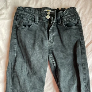 Svarta jeans från Gina Tricot, strl 158 - Snygga svarta jeans från Gina Tricot med klassisk femficksdesign och silverfärgade knappar. Jeansen har en rak passform och är tillverkade i mjukt denimtyg. Perfekt för dig som gillar stilrena och enkla jeans med diskreta detaljer.