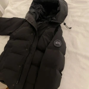 Canada Goose black label - Säljer en svart pufferjacka från Canada Goose med stor huva och snygg patch på ärmen. Jackan har dragkedja och tryckknappar framtill, samt justerbar snörning vid huvan. Perfekt för kalla dagar och riktigt stilren look. Dm för mer info