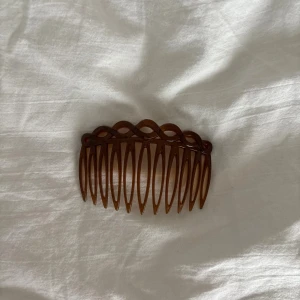 Brun hårkam med vågig kant - Snygg brun hårkam i plast med vågig och flätad design längs kanten. Perfekt för att fixa frisyren och ge en retro touch till din look. Lätt att använda och sitter bra i håret. Passar både till utsläppt och uppsatt hår.