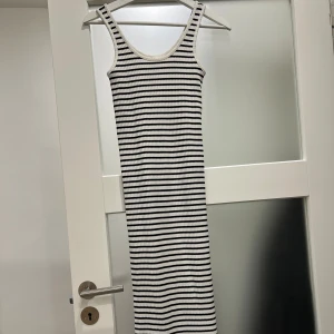 Randig långklänning XS/S - Säljer en ribbad långklänning i storlek XS/S. Klänningen är ärmlös med rund hals och har ett stilrent svartvitt randigt mönster. Materialet är mjukt och stretchigt, perfekt för dig som gillar en slim passform och enkel, modern look.