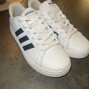 Vita Adidas sneakers med svarta ränder - Snygga vita Adidas sneakers med klassiska svarta ränder på sidorna och vit sula.         Storlek 36 2/3. Endast provade då de inte passade dottern