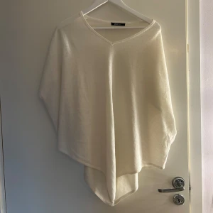 Vit poncho från Gina Tricot  - Supermjuk och stilren vit poncho från Gina Tricot i ullblandning. Ponchon har v-ringad hals och en lös, flowy passform som ger en chill och avslappnad vibe. Bra skick! 
