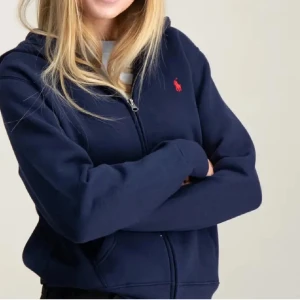 Marinblå hoodie från Ralph Lauren - Mysig marinblå hoodie från Ralph Lauren med dragkedja framtill och klassisk röd logga på bröstet. Tröjan har huva och långa ärmar. Tröjan är i storlek 152 men passar en XS‼️‼️💞