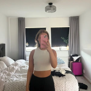 Vit croppad linnetopp - Säljer en vit croppad linnetopp med rund halsringning och ärmlös design. Toppen är ribbad och sitter tight mot kroppen, perfekt för varma dagar eller att styla med höga byxor. Enkel och stilren look som passar till mycket.