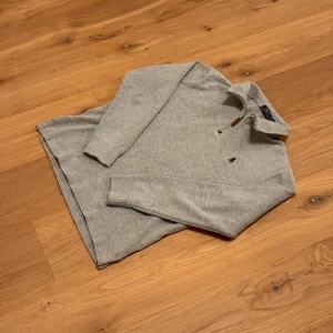 Grå half zip tröja från Polo Ralph Lauren - Säljer en stilren grå tröja från Polo Ralph Lauren med half zip och klassisk krage. Tröjan har lång ärm, broderad logga på bröstet och är gjord i mjuk bomull. Perfekt för lager-på-lager och chill vardagsstil.