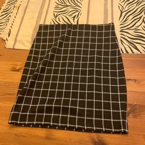 Svartvit rutig minikjol XS - Snygg svart minikjol med vitt rutmönster från Cubus i storlek XS. Kjolen har en rak och tight passform och är perfekt för dig som gillar en stilren och trendig look. Tyg i mjuk och bekväm polyesterblandning.