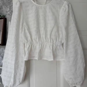 Vit blus med puffärmar och struktur - Säljer en vit blus med lång puffärm och markerad midja. Blusen har ett subtilt rutigt strukturmönster i tyget och  volang nertill. Perfekt för dig som gillar romantisk och trendig stil.