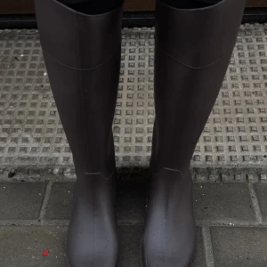 Bruna höga stövlar i syntet - Snygga, höga bruna stövlar med stilren design. De är tillverkade i syntetmaterial och har en klassisk, rund tå och platt sula. Perfekta för att lyfta din outfit under höst och vinter. Helt oanvända 