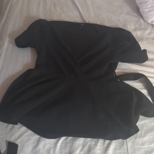 Svart omlottklänning med puffärm - Svart kort omlottklänning från H&M med puffiga korta ärmar och knytband i midjan. Klänningen har en v-ringad hals och en flowy kjol. Den är oanvänd , om du vill se hur den ser ut på mig skriv till mig💕