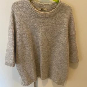 Beige stickad tröja/ t shirt från Gina Tricot - Mysig beige stickad tröja från Gina Tricot med rund halsringning och trekvartsärm. Tröjan har en avslappnad passform och ribbade muddar vid ärmslut och nederkant. Perfekt för lager-på-lager under kyliga dagar.