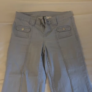 Ljusblå cargopants med fickor - Säljer ett par ljusblå cargopants med snygga fickor framtill och breda hällor. Byxorna har låg midja och raka ben. Perfekta om du gillar en chill och trendig stil. Materialet känns som bomull och de har knapp- och dragkedjestängning.