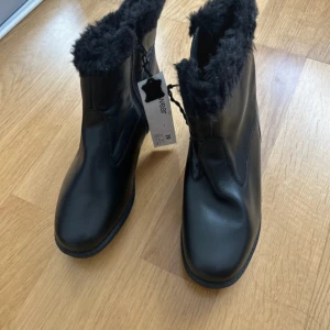Svarta boots med fuskpäls, storlek 39 - Svarta boots i skinnimitation med mjukt foder av svart fuskpäls. Snygg och enkel design med rund tå och platt sula. Perfekta för kalla dagar när du vill hålla stilen och samtidigt vara varm. Dragkedja på sidan för enkel påtagning.