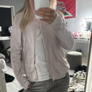 Ljusrosa kofta med knappar - Säljer en ljusrosa kofta med knappar framtill. Koftan har långärmad design och är tillverkad i ett mjukt, strukturerat material som känns skönt mot huden. Perfekt att slänga över en t-shirt för en chill och snygg look.