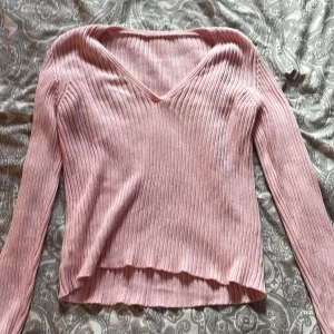 Rosa ribbad långärmad tröja - Säljer en ljusrosa ribbad tröja med v-ringning och långa ärmar. Tröjan är figurnära och har en mjuk, stretchig känsla. Perfekt för lager-på-lager och passar till både jeans och kjol.