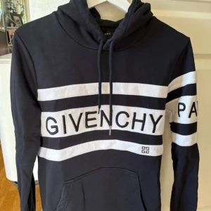 Svart och vit hoodie från Givenchy - Pris kan diskuteras. Säljer en äkta svart hoodie från Givenchy med vita ränder och stor logga över bröstet. Tröjan har huva med snörning, känguruficka och långa ärmar med vita detaljer och text på ena ärmen. Perfekt för dig som gillar streetstyle och exklusiva märken.