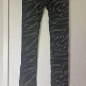 Svarta kamouflagemönstrade leggings/långkalsonger - Snygga svarta leggings från Lindex med mörkgrått kamouflagemönster.. Mjukt och stretchigt material som sitter skönt på kroppen. Perfekta för roliga aktiviteter i kyligt väder. Resår i midjan och mudd vid benslut.
