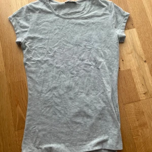 Ljusgrå t-shirt från Vila XS - En basic ljusgrå t-shirt från Vila i storlek XS. T-shirten har rund halsringning och korta ärmar. Den är gjord i mjuk bomull och har en slim passform som sitter snyggt på kroppen. Perfekt att matcha med jeans eller kjol.
